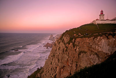 View of lighthouse at seaside during sunset