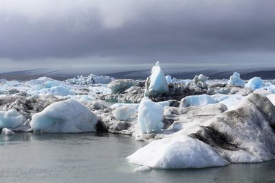 Snow covered landscape by sea against sky