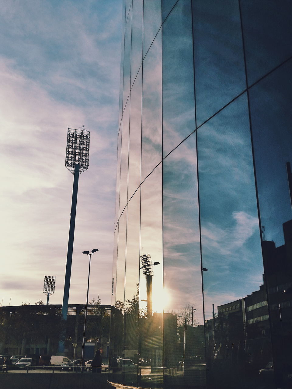 built structure, architecture, building exterior, sky, city, low angle view, cloud - sky, car, transportation, sunlight, sunset, land vehicle, street, sun, sunbeam, cloud, building, modern, mode of transport, city life