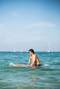 Full length of shirtless man in sea against sky