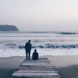 Rear view of men standing at beach against cloudy sky