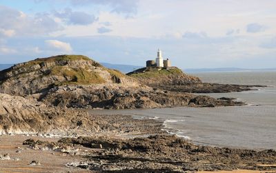 Lighthouse on beach by sea against sky