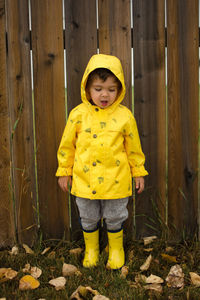 Full length of boy in raincoat standing against fence