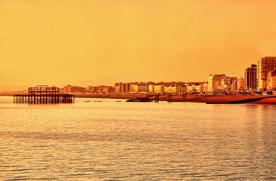 Sea by buildings against clear sky during sunset