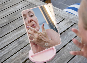 A middle-aged woman applying a cleansing scrub to her face in front of a mirror