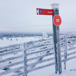 Road sign on snow covered landscape against sky