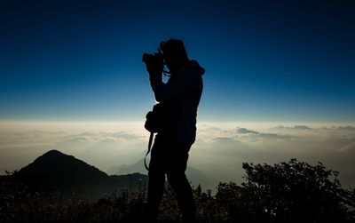 Silhouette male hiker photographing while standing on mountain during sunset