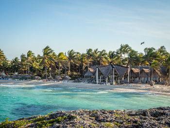 Beach huts by palm trees against sky