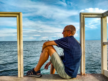 Man sitting by sea against sky