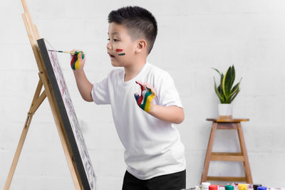 Side view of boy painting on canvas at home
