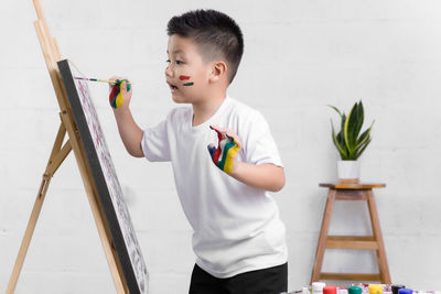 Boy holding paper while standing against white wall