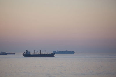 Commercial ships anchored at sea at sunset.