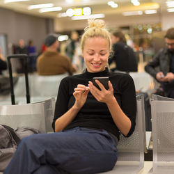 Smiling woman using phone sitting at airport