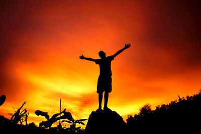 Silhouette man with arms outstretched standing against orange sky