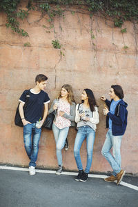 Full length of teenagers talking while leaning on wall