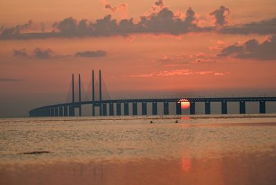 Bridge over sea against orange sky