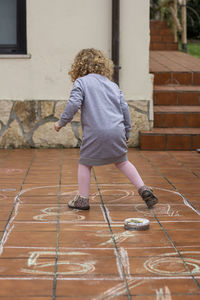 Curly blonde girl playing hopscotch in the backyard