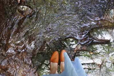 Low section of woman standing on rock by water