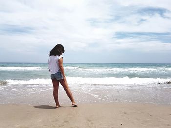 Rear view of young woman standing at seashore against sky