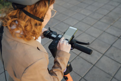 Redhead businesswoman using mobile phone on electric push scooter