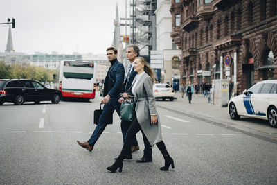 Businesswoman with male colleagues crossing road in city