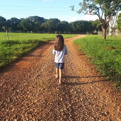 Rear view of woman walking on road amidst field