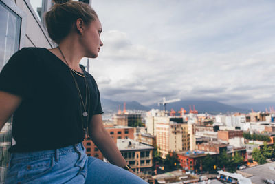 Young woman sitting on city against sky