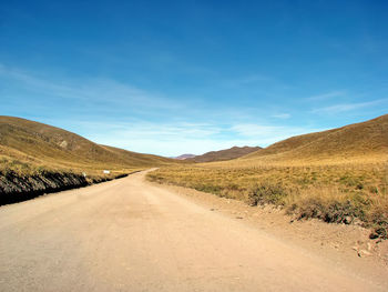 Dirt road along countryside landscape against blue sky