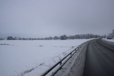 Snow covered road by trees against sky