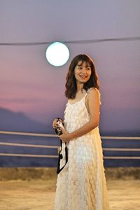 Portrait of smiling young woman standing against sky