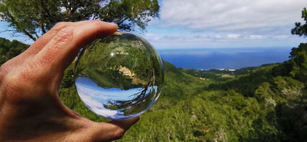 Cropped hand holding crystal ball against sky