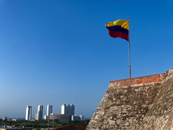 Low angle view of flag against buildings against clear blue sky