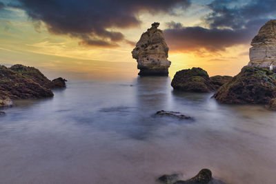 Rocks in sea against sky during sunset