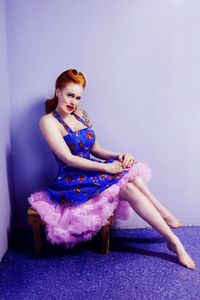 Portrait of young woman sitting against blue wall