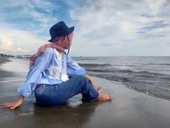 Young woman sitting on beach against sky