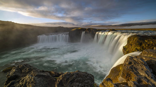 Scenic view of waterfall against sky during sunset