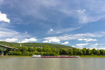 A barge flowing on the river rhine  with a blue sky with clouds and a forest in the background.