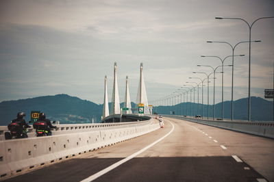 Road by suspension bridge against sky