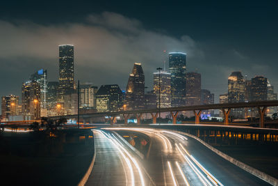 Illuminated street amidst buildings against sky at night