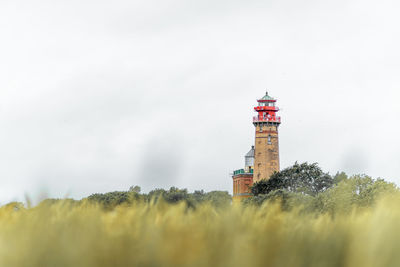 Lighthouse on field by building against sky