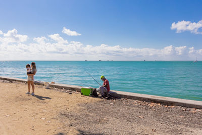 Men sitting on beach against sky
