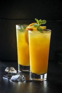 Two glasses of orange drink with ice cubes on black surface