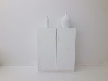 Close-up of white bottles on table against wall