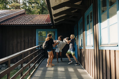 Cheerful children playing with pillows in corridor near cabin at summer camp