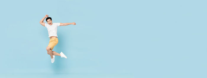 Full length of woman jumping against clear blue sky