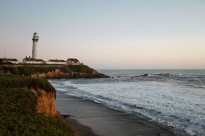 Lighthouse by sea against clear sky