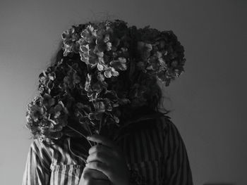 Woman holding flower bouquet over face against white wall