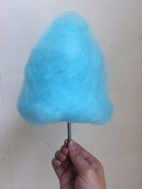 Close-up of hand holding blue cotton candy over white background