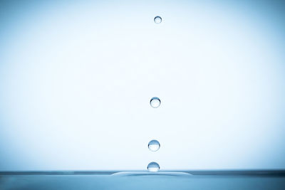 Close-up of drop falling in blue water against white background