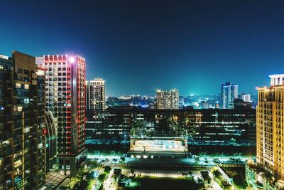 Illuminated cityscape against clear blue sky at night